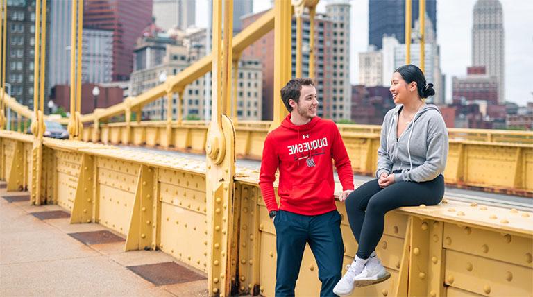 female and male student in Duquesne gear on Rachel Carson Bridge Pittsburgh